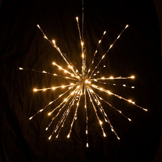 A starburst-style light fixture hangs against a dark background. The light features multiple radiating rods, each tipped with a small bulb, creating a glowing, spherical shape reminiscent of a firework or star.