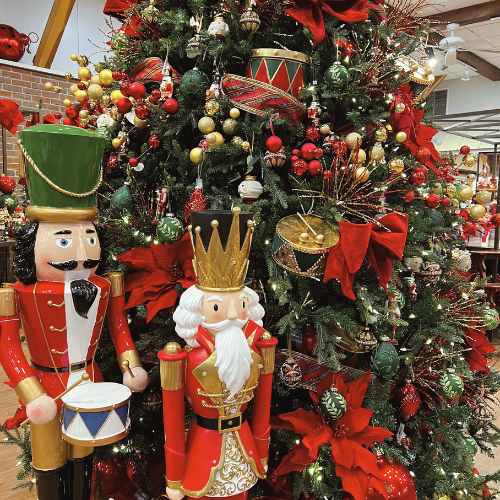 A festive Christmas tree decorated with red poinsettias, gold ornaments, drums, and garlands, with two large nutcracker figures—one with a green hat and one with a gold crown—standing in front.